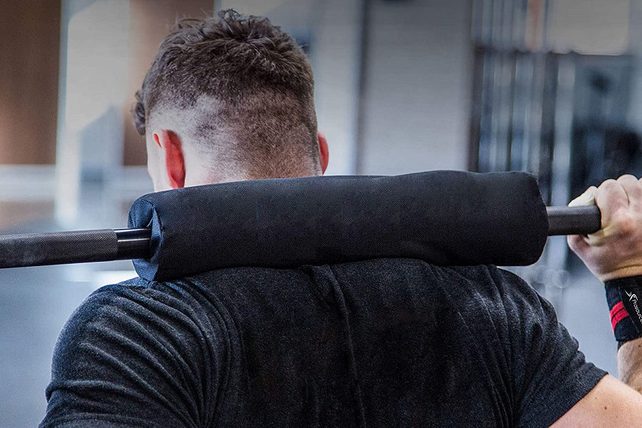 Black foam shoulder pad on barbell with red ear detail visible, worn by model during squat exercise