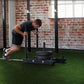 Man pushing black sled on bright green synthetic turf in industrial gym space with brick walls