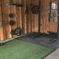 Green rubber gym turf with black edges on concrete floor in home gym space with wooden walls and weight equipment