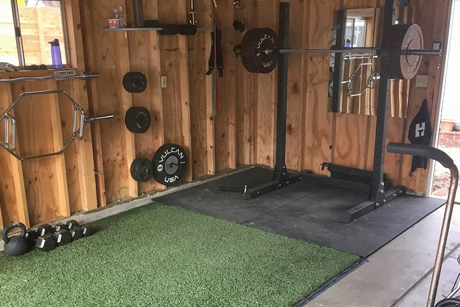 Green rubber gym turf with black edges on concrete floor in home gym space with wooden walls and weight equipment