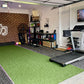 Bright green artificial turf flooring in home gym space with treadmill, exercise equipment, and brick wall
