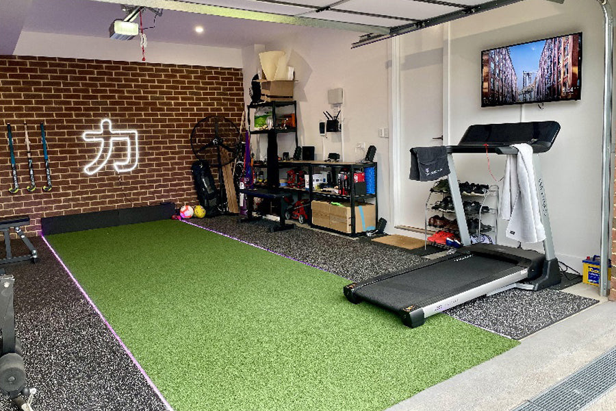Bright green artificial turf flooring in home gym space with treadmill, exercise equipment, and brick wall