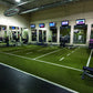 Green synthetic turf sports field with white yard line markings in indoor gym facility