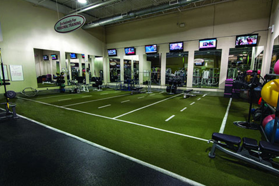 Green synthetic turf sports field with white yard line markings in indoor gym facility