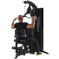 Black multi-station home gym with leg press, man in black shirt demonstrating lat pulldown exercise on white background