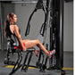 Woman using black multi-station home gym machine with leg press attachment in gym setting