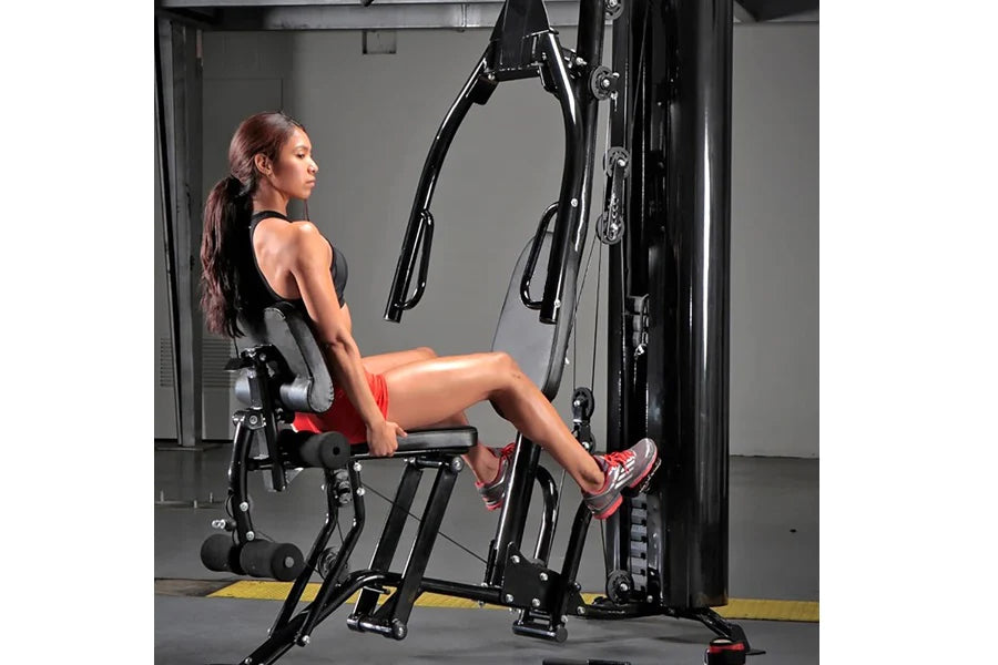 Woman using black multi-station home gym machine with leg press attachment in gym setting