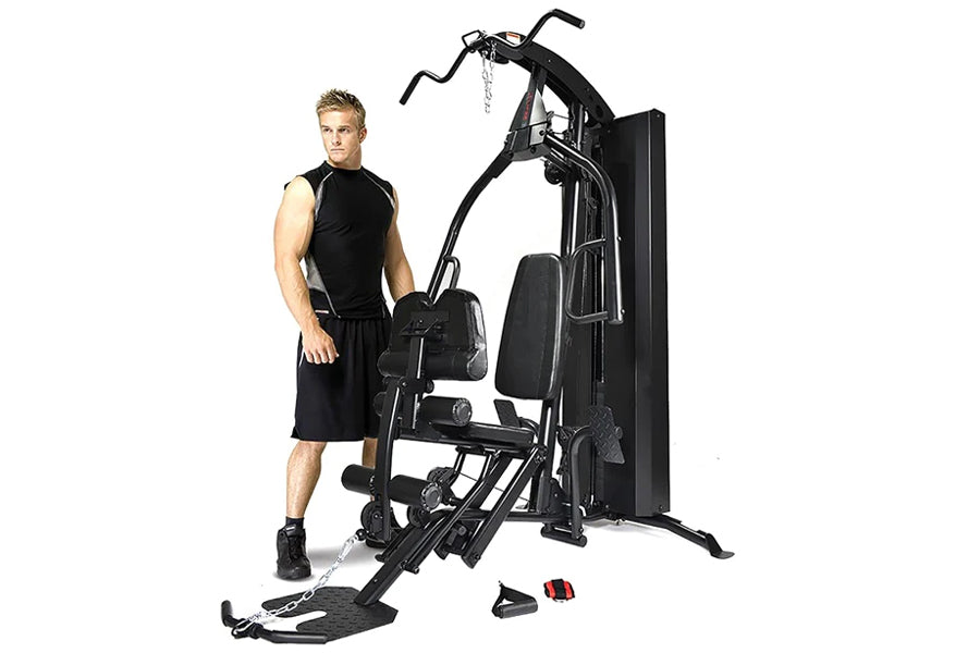 Man in black sleeveless shirt standing next to black multi-station home gym equipment with leg press and padded seat