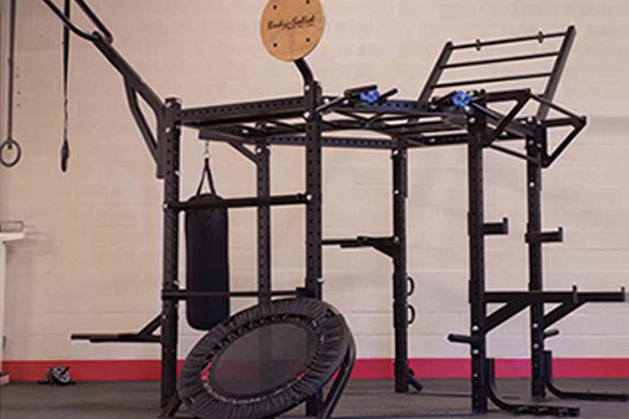 Black metal hexagon multi-function gym rig with pull-up bar, with rebounder trampoline and heavy bag attachment in workout sp