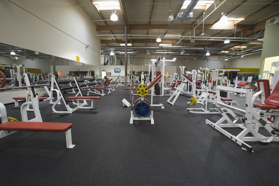 Warrior Interlocking Rubber Gym Flooring Tiles in speckled black, installed in commercial fitness facility with exercise equi