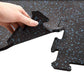 Hand holding black interlocking rubber gym floor tile with blue speckles, shown over white background