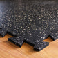 Black rubber gym tile with white speckle pattern and interlocking edges, shown on wood floor