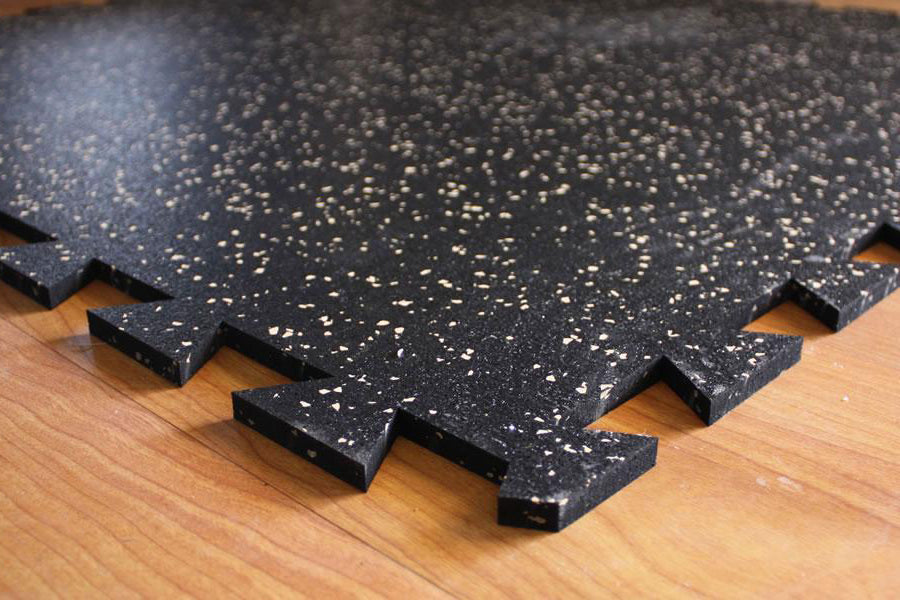 Black rubber gym tile with white speckle pattern and interlocking edges, shown on wood floor
