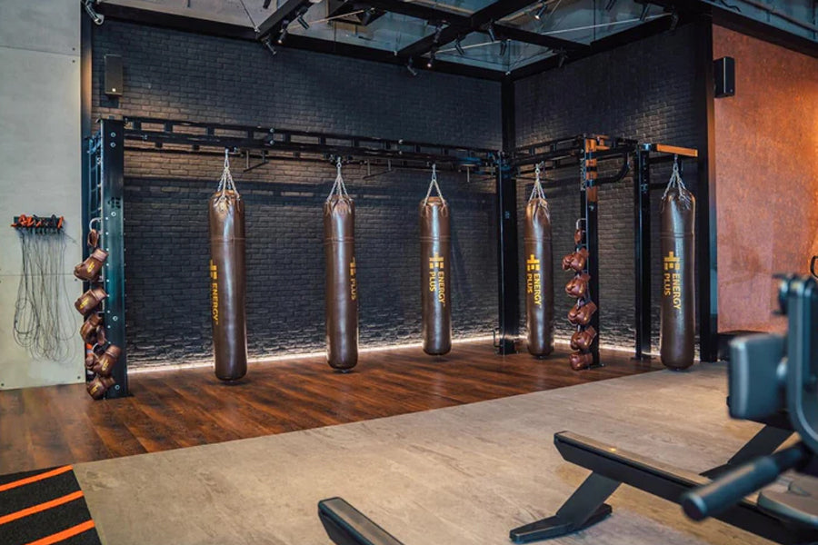 Modern boxing gym interior with five brown heavy punching bags suspended from black ceiling rig against dark brick wall, wood
