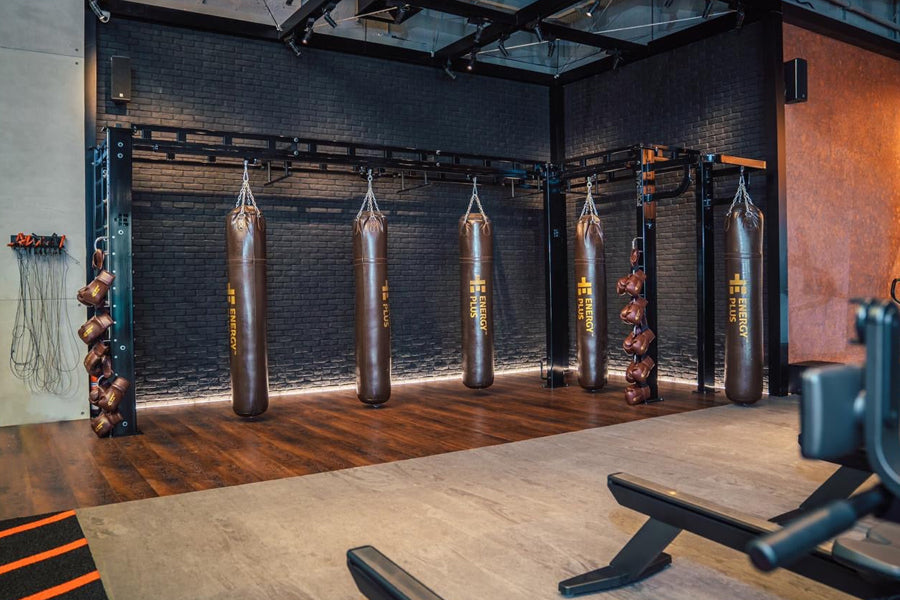 Modern gym studio with gray interlocking tiles, heavy punching bags, brick walls, and wooden flooring