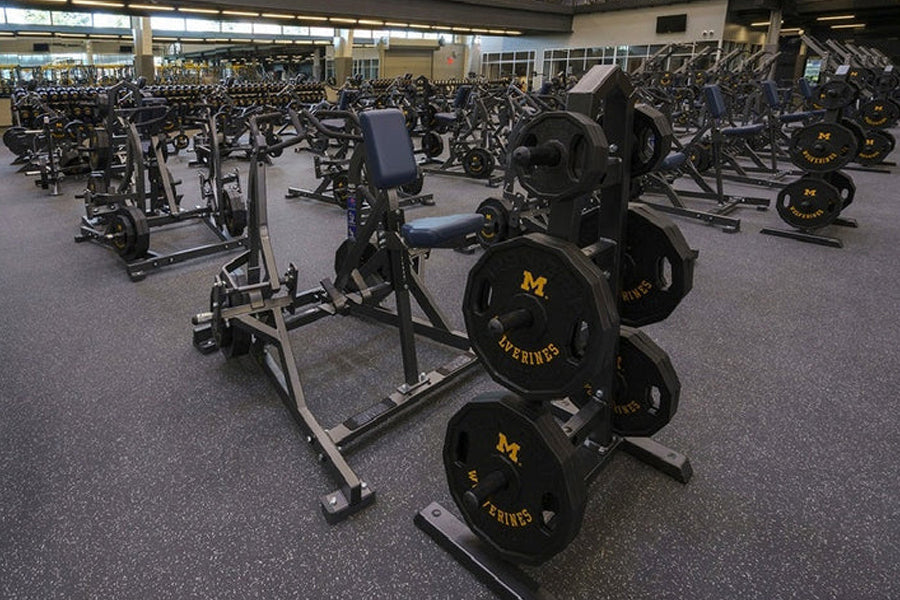 Gym floor view showing interlocking rubber tiles with black weight plates and stationary bikes in fitness facility