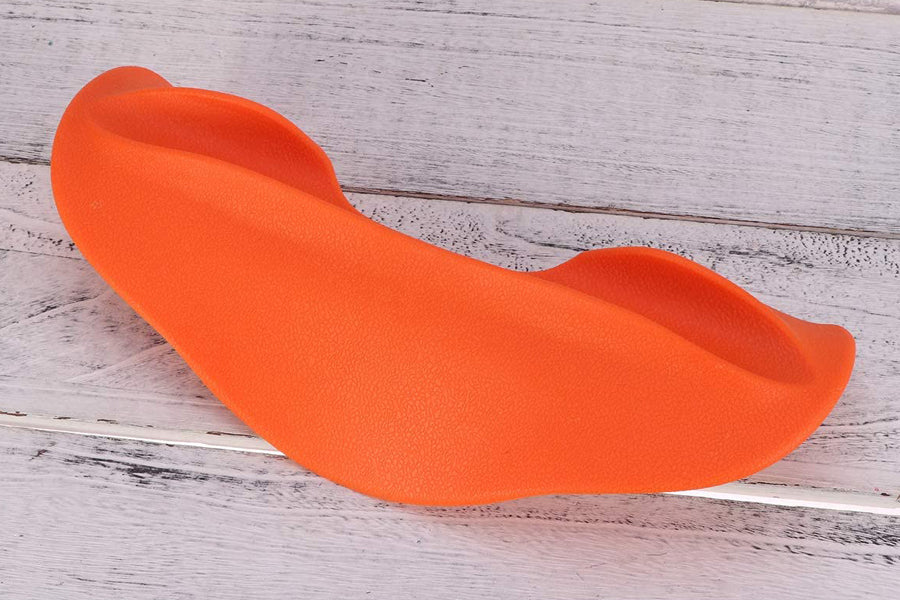 Bright orange foam squat pad with curved design and handles, displayed on whitewashed wood background