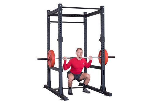 Black power rack with red weight plates and barbell, man in red shirt performing squat exercise