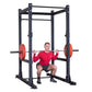 Black power rack with perforated uprights, red weight plates on loaded barbell, man in red shirt performing squat exercise
