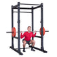 Man performing squat exercise with red weight plates on black steel power rack with perforated uprights