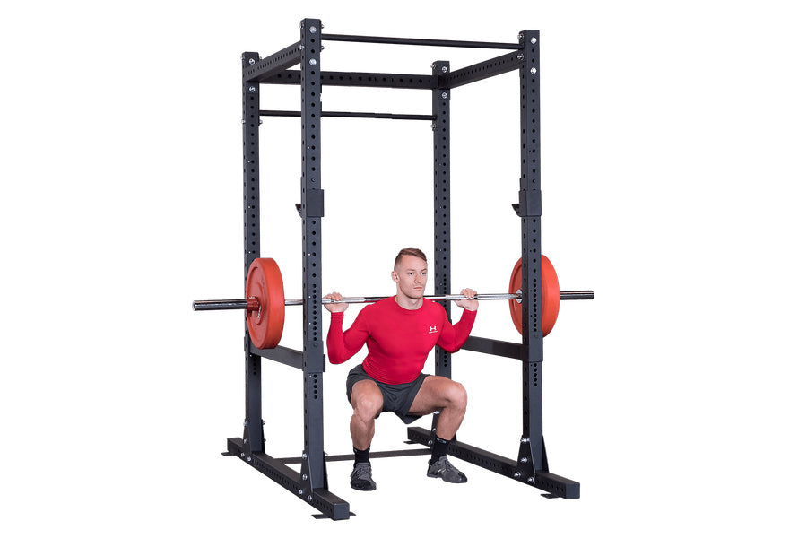 Man performing squat exercise with red weight plates on black steel power rack with perforated uprights