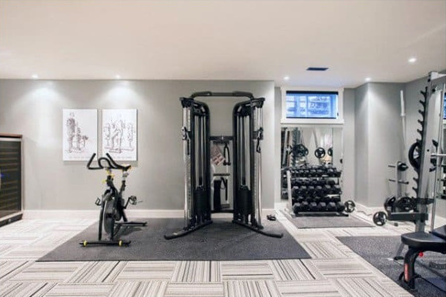 Warrior rubber gym floor mats in charcoal gray, shown installed in modern home gym with exercise equipment on light wood-look