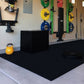 Black rubber gym floor mat with yellow kettlebell and weight plates on wall-mounted rack in fitness studio setting