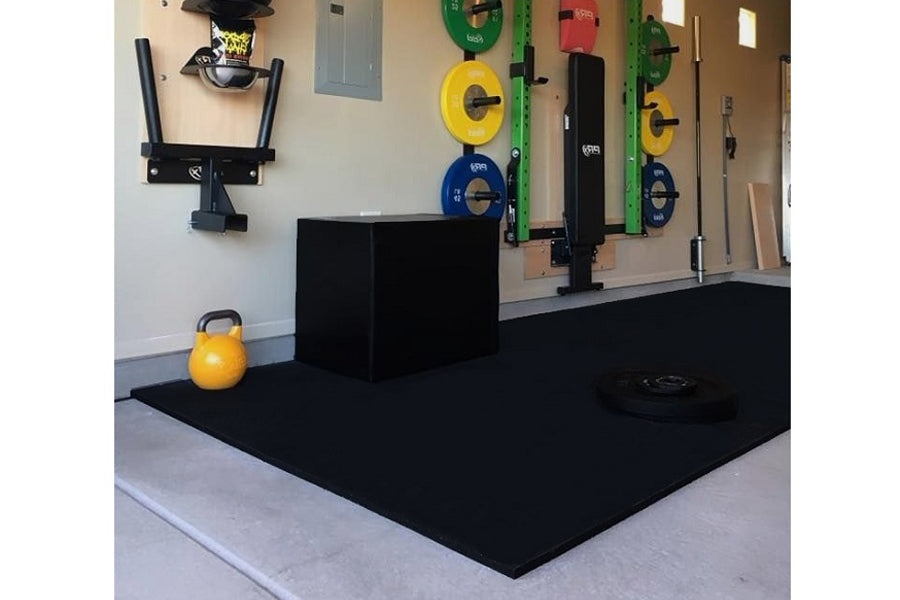 Black rubber gym floor mat with yellow kettlebell and weight plates on wall-mounted rack in fitness studio setting
