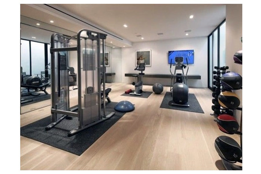 Modern home gym interior with light wood flooring, featuring Warrior Rubber Gym Floor Mats in black under exercise equipment 