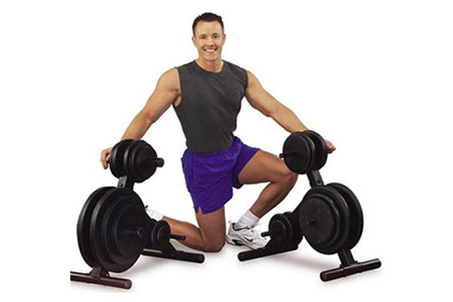 Man in charcoal sleeveless shirt and purple shorts holding dumbbells, posed with Warrior Standard Plate Tree dumbbell rack on