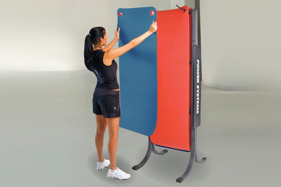 Woman in black athletic wear standing beside blue and red padded wall-mounted mats on dark frame rack