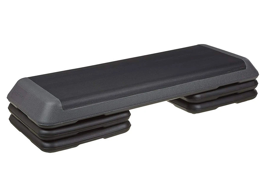 Black aerobic stepper platform with gray padded top and adjustable risers on white background