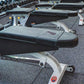 Row of black and gray roof rack systems with metal brackets and yellow adjustment knobs displayed on gray gym flooring