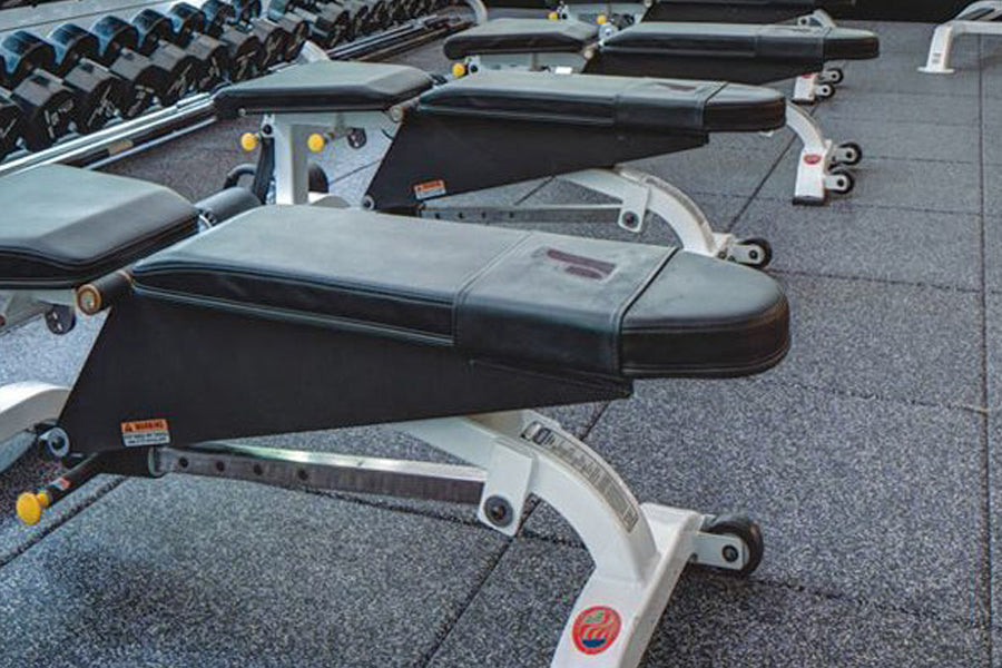 Row of black and gray roof rack systems with metal brackets and yellow adjustment knobs displayed on gray gym flooring