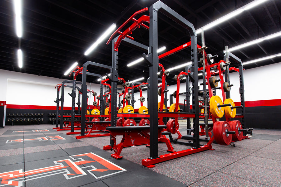 Commercial gym flooring with red and black rubber tiles installed in modern fitness facility with red weight racks