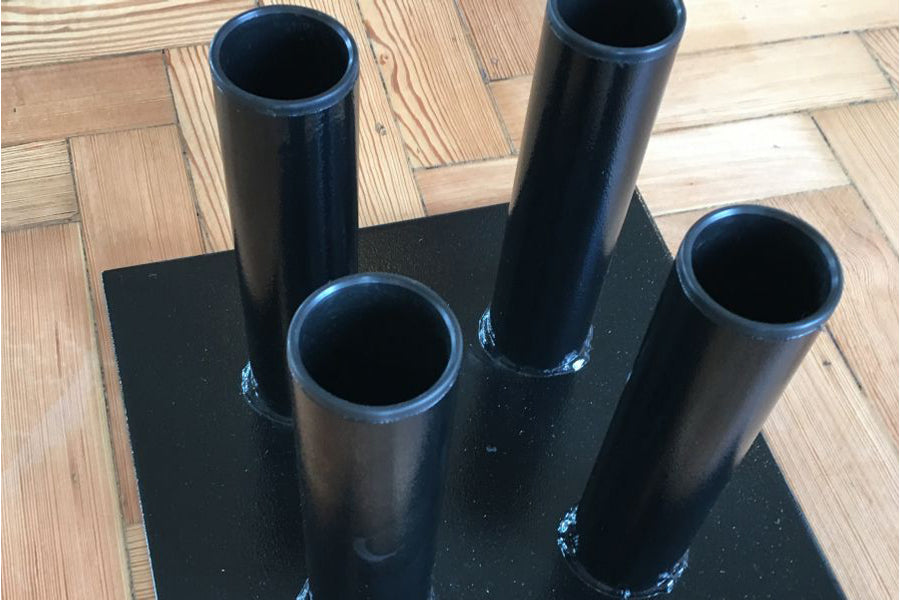 Warrior Vertical Floor 4 Olympic Bar Holder with four black steel tubes mounted on black base, on wooden floor