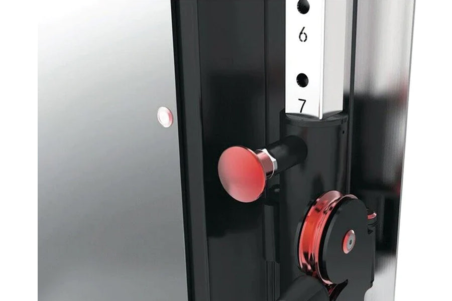 Black and red wall-mounted cable pulley gym system with red weight stack and numbered guide rod on white background