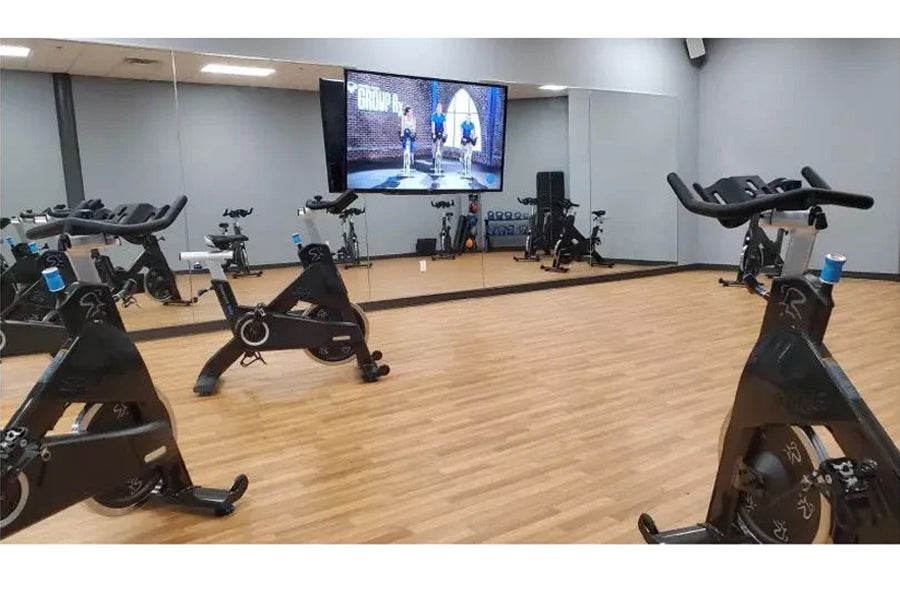 Warrior Wood Grain Interlocking Gym Flooring Tiles in light oak finish shown in fitness studio with stationary bikes