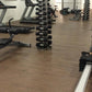 Warrior wood grain interlocking gym flooring tiles in brown, displayed in fitness studio with gym equipment