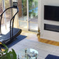 Woodway Curve Treadmill with black frame and blue mat in modern home gym setting with glass doors and wall-mounted TV