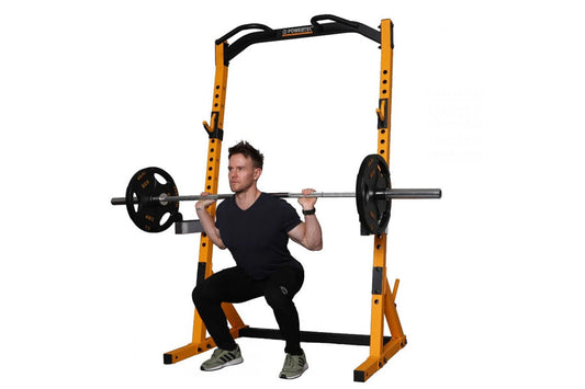 Yellow and black Powertec half rack with adjustable safety arms, shown with model performing barbell squat exercise