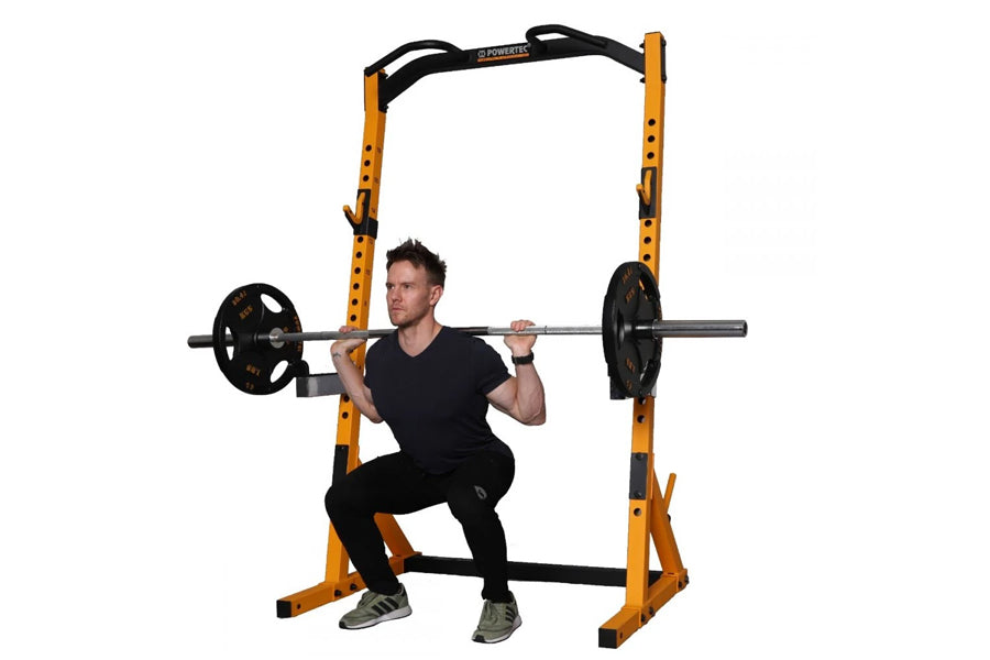 Yellow and black power rack with adjustable safety bars, model shown with man in squat position holding barbell with weight p