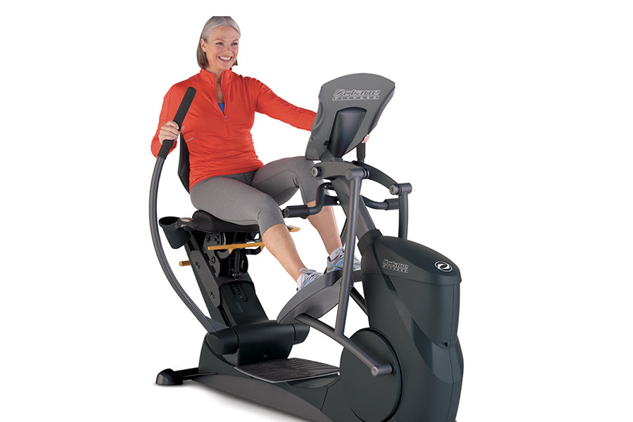 Woman in red jacket and gray capris using black and gray commercial recumbent elliptical machine on white background