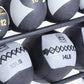 Black and gray medicine balls with weight labels and cross-stitching displayed on black metal rack, white background