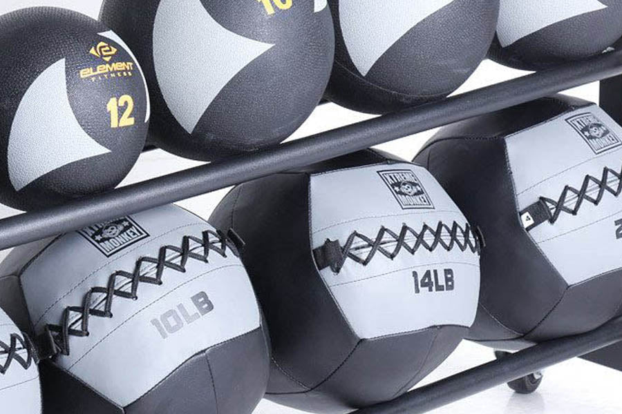 Black and gray medicine balls with weight labels and cross-stitching displayed on black metal rack, white background