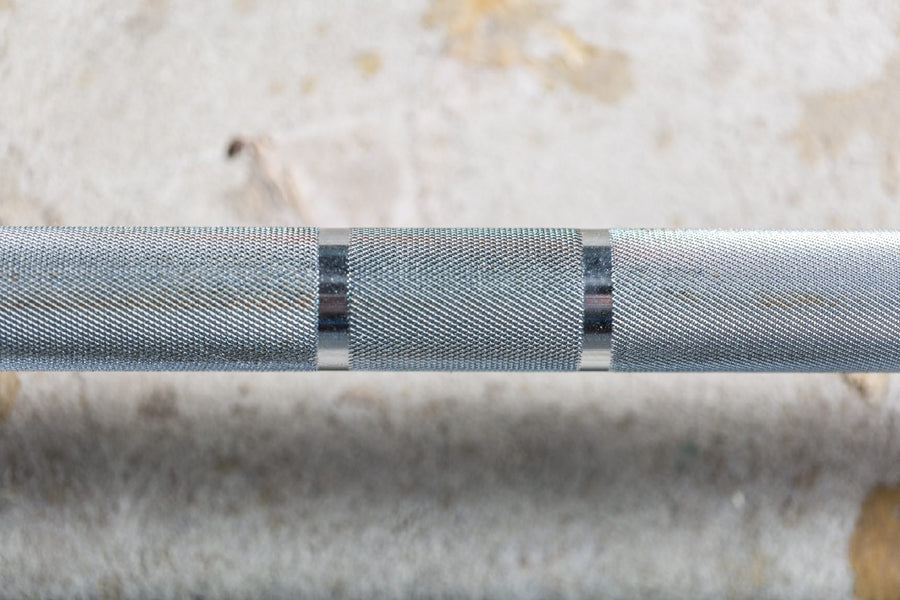 Gray knurled Olympic barbell with black grip bands, close-up detail on textured surface