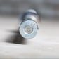 Silver metal Olympic barbell end cap with circular center design, shown from front view on white surface
