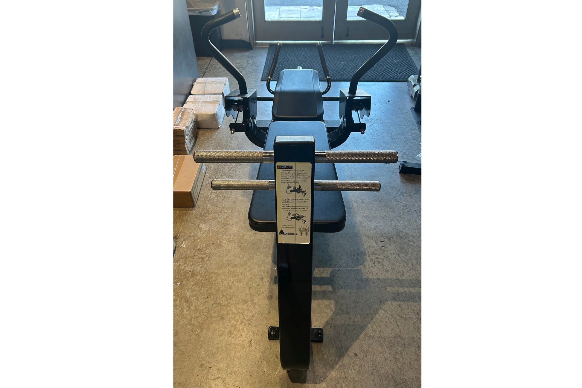 Black and silver commercial abdominal bench with curved handles and foot pedal, viewed from above in gym setting