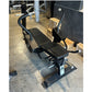Black abdominal exercise bench with padded seat and backrest, curved handles, and weighted leg press attachment on concrete f