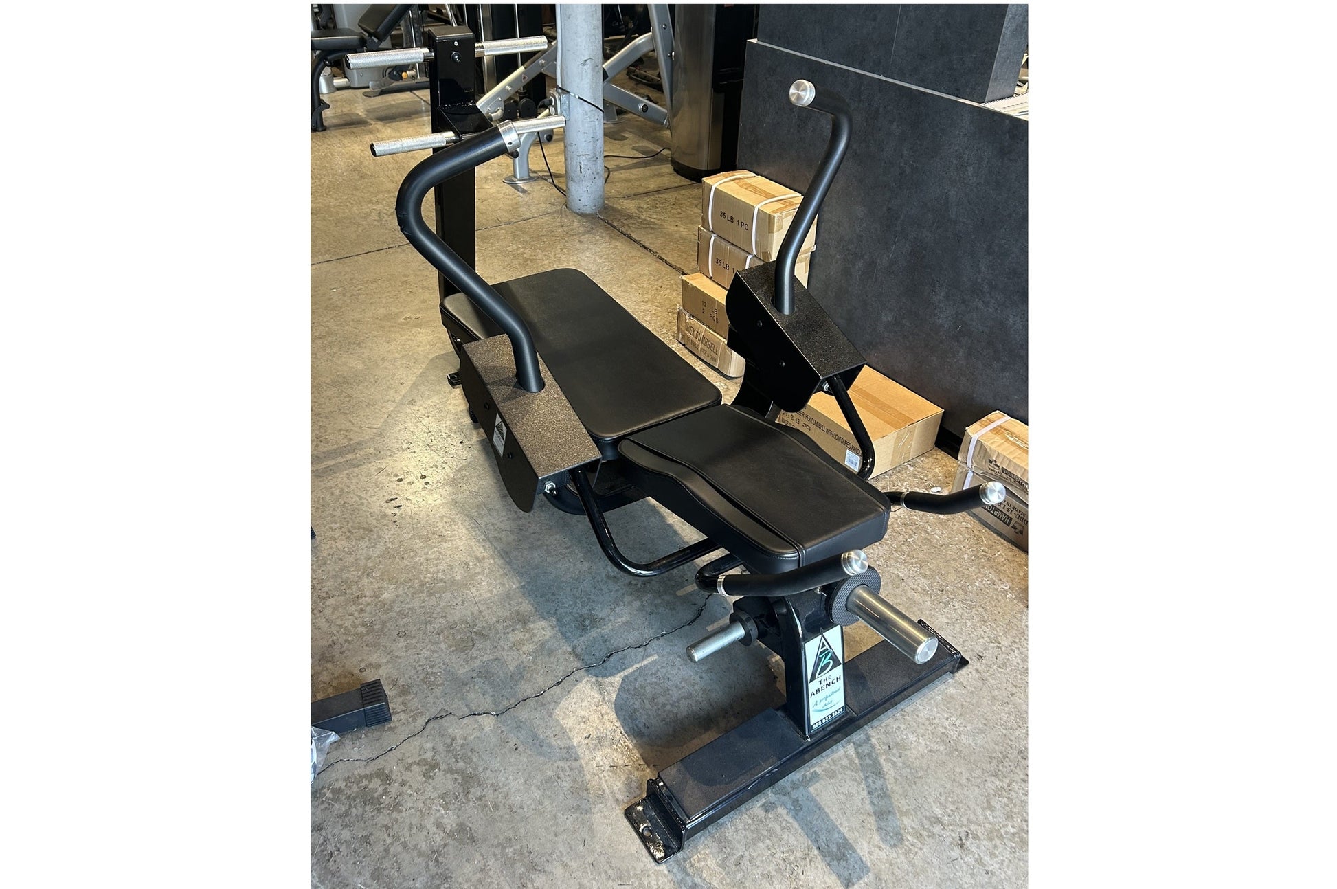 Black abdominal exercise bench with padded seat and backrest, curved handles, and weighted leg press attachment on concrete f
